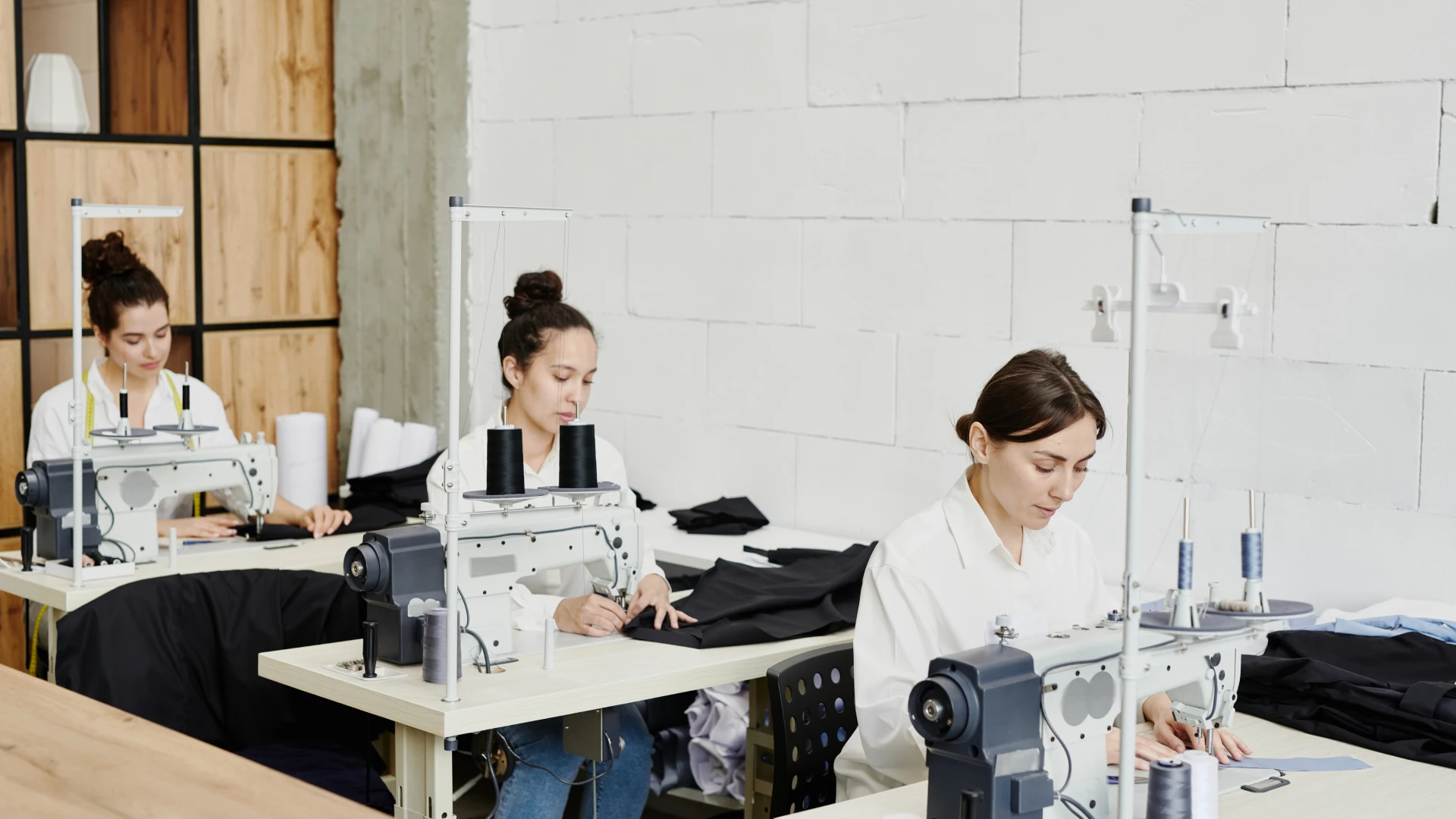 row-young-seamstresses-sitting-by-desks-using-electric-sewing-machines-while-working-new-seasonal-collection